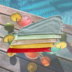 Set of five Turbie Twist hair towels. Colors are blue, aqua, tan, yellow and coral. In the background, there is a photo of a pool and colorful cocktails.